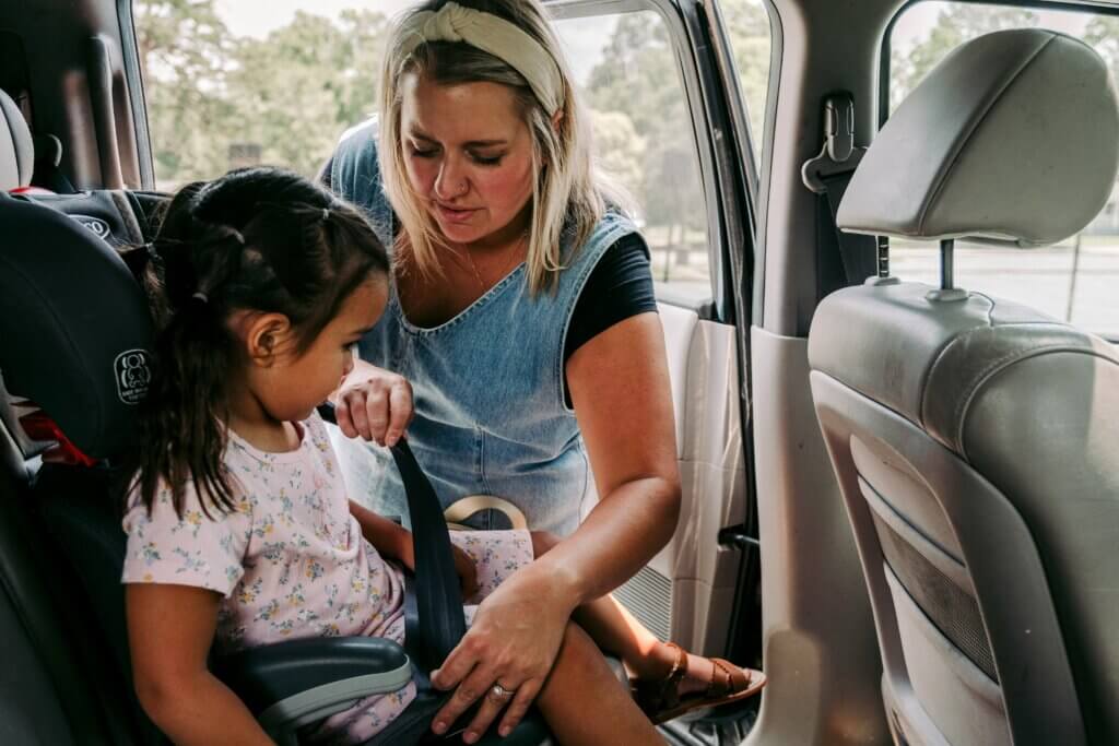 Woman putting a preschooler in a carseat